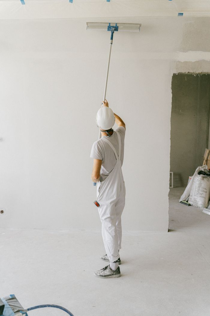 The Art of Drawing Readers In: Your attractive post title goes here Back view of a painter in overalls and hard hat painting an interior wall with a roller.