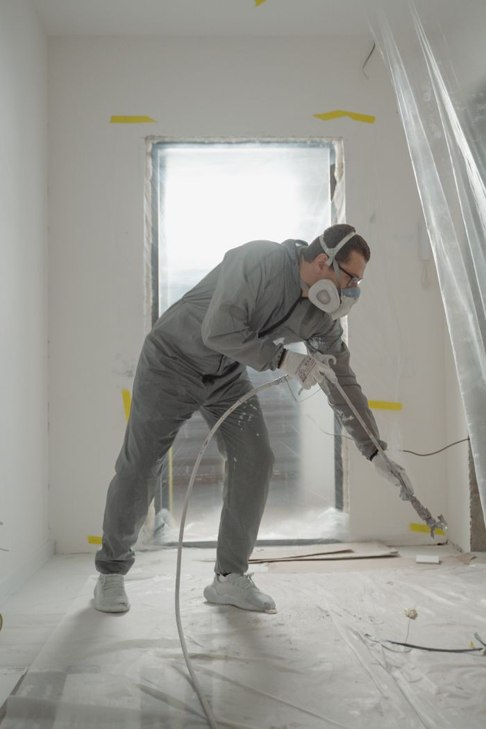 contact-img Worker applying paint with a spray gun in a protected indoor renovation site.